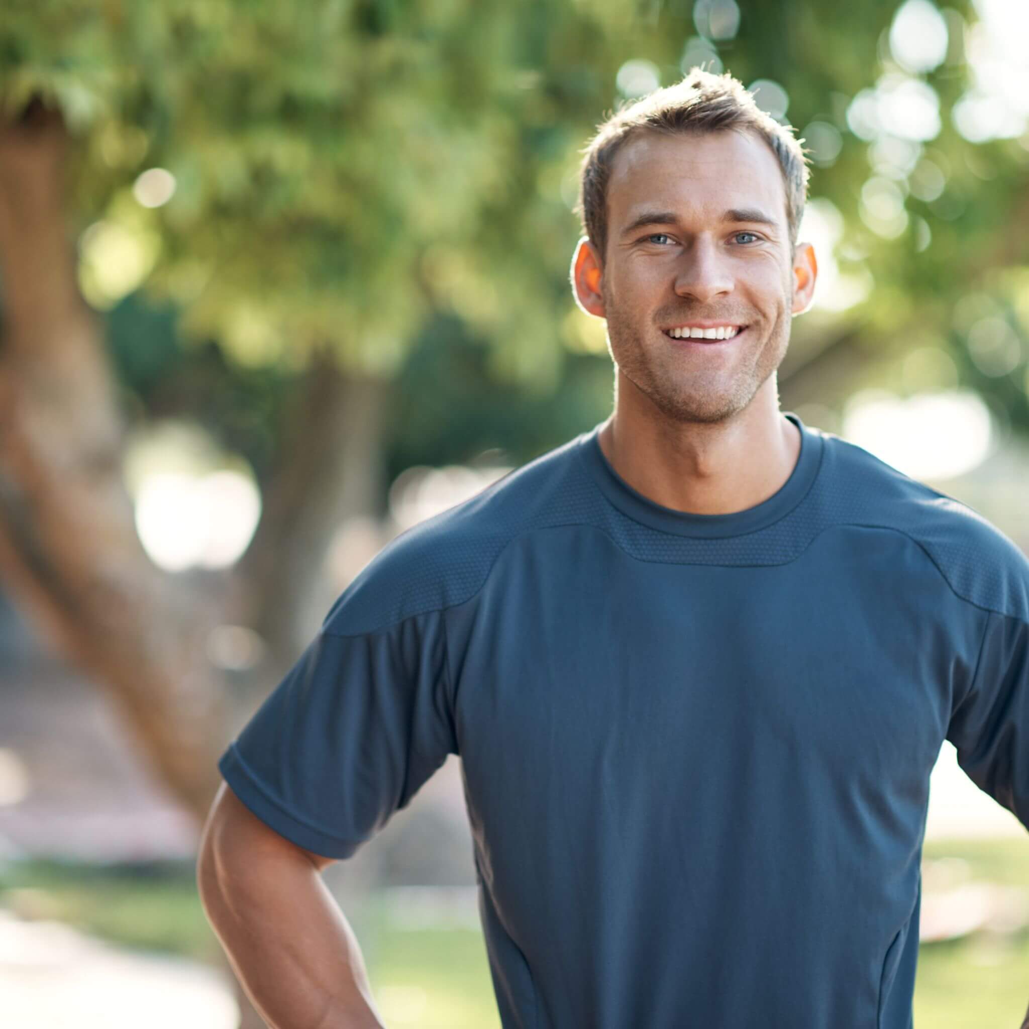 A man wearing a blue shirt with a blurred green outdoor background with full arch implants