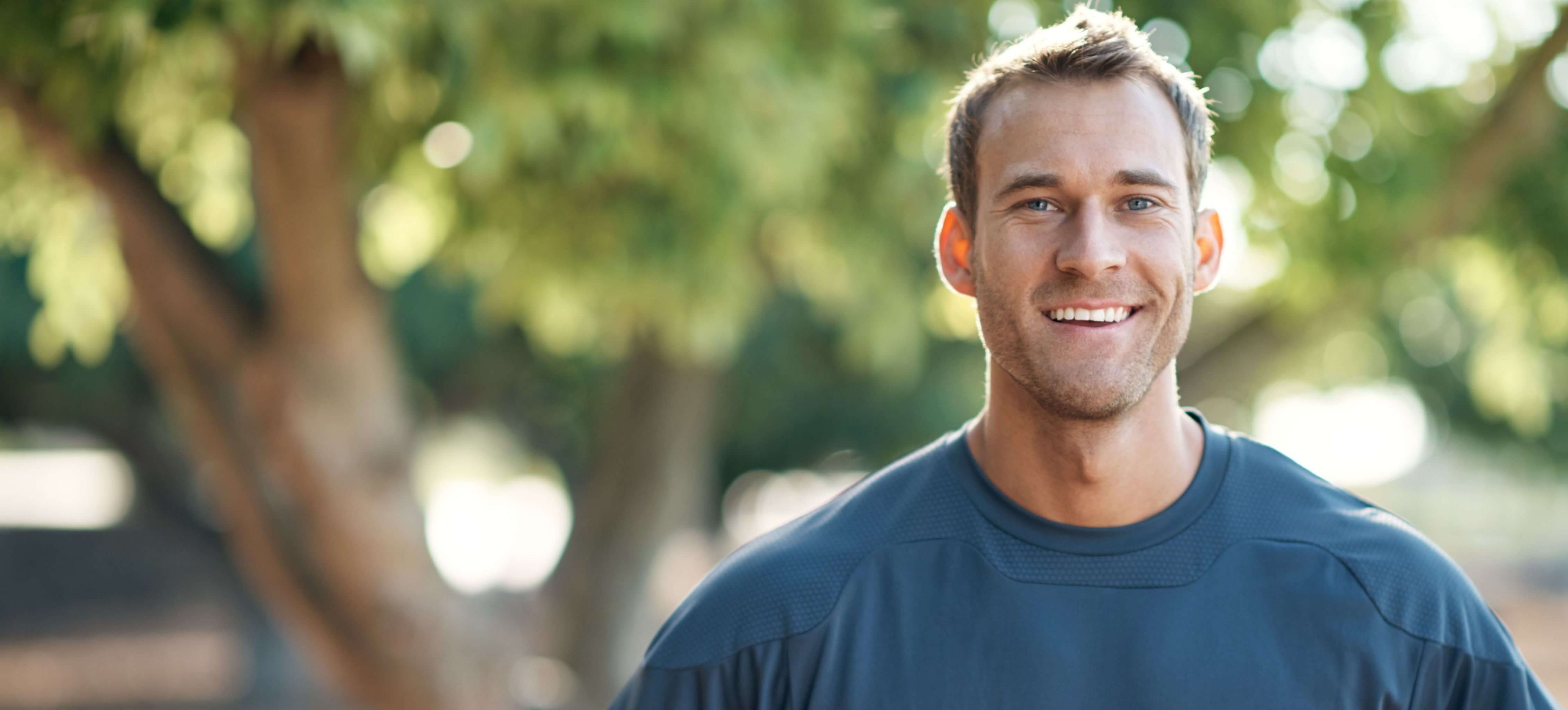 A man wearing a blue shirt with a blurred green outdoor background with full arch implants