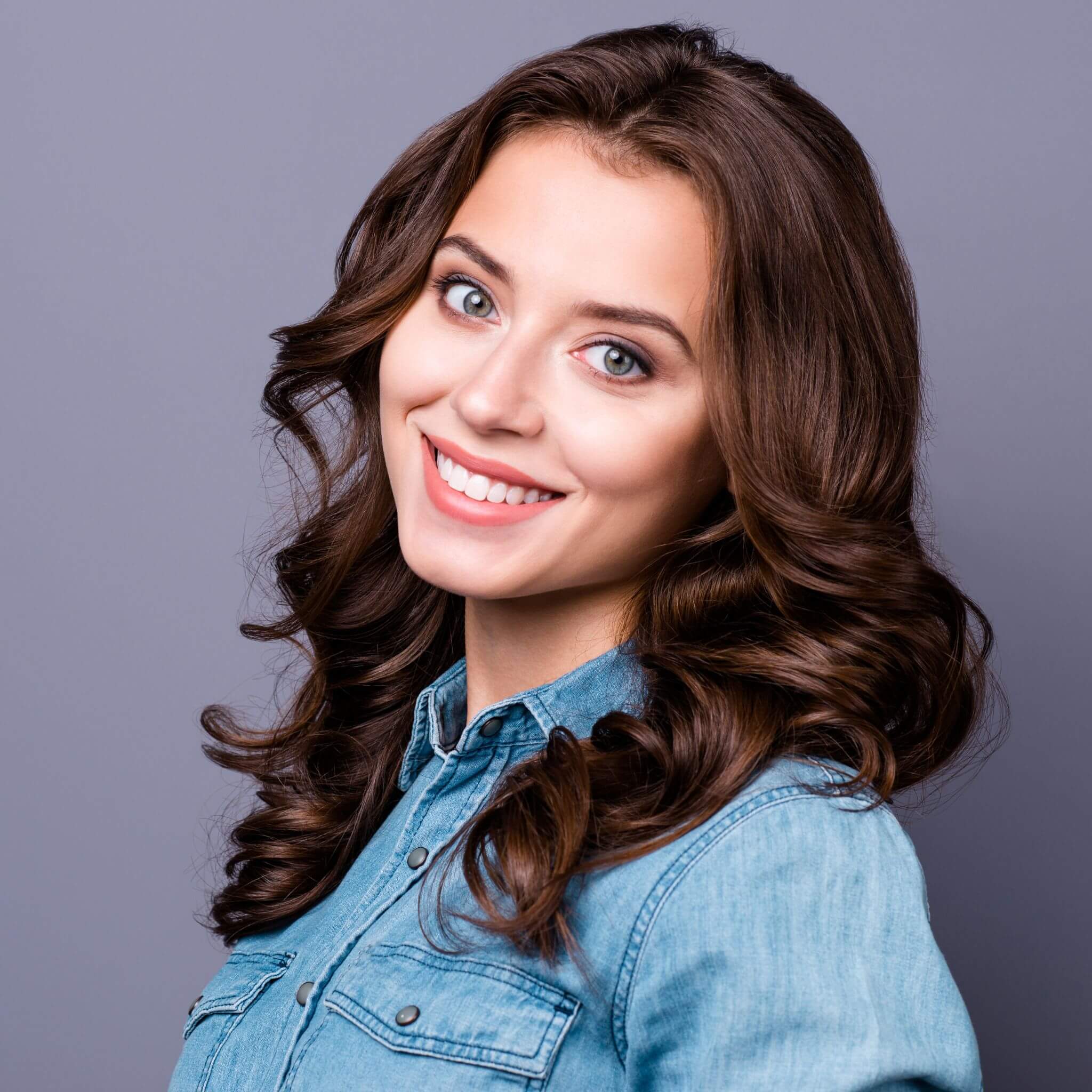 Woman with a single dental implant smiling against a grey - purple background