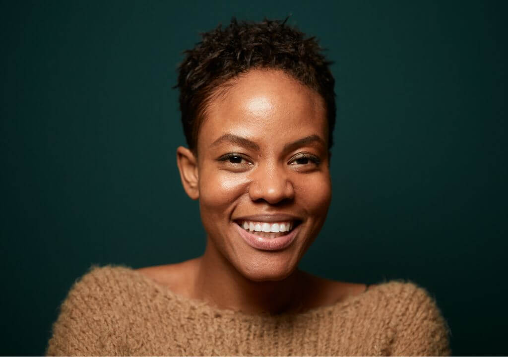 Woman smiling with a single dental implant wearing a brown sweater against a dark green background