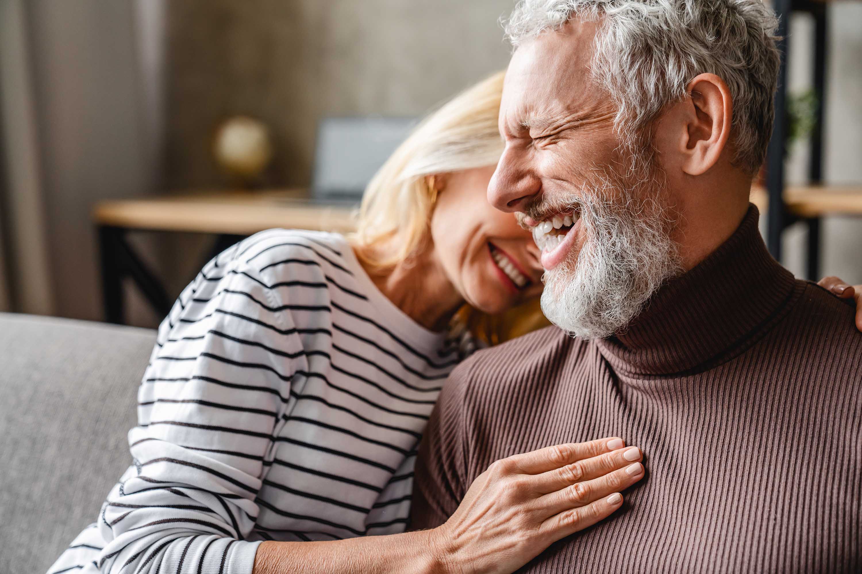 Happy elderly couple laughing together in a cozy living room.